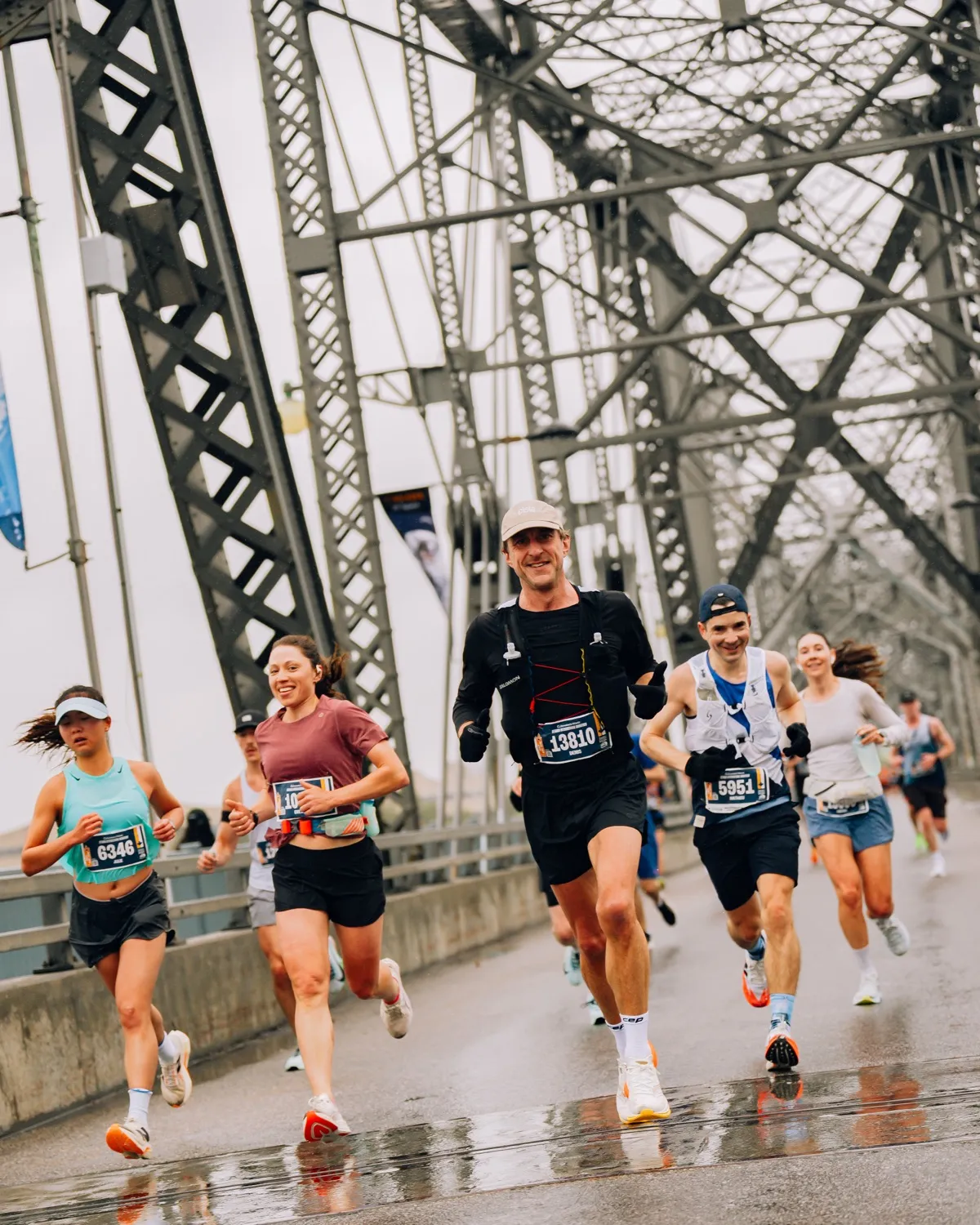 Corredores sonrientes del maratón de Ottawa cruzando un puente de acero bajo la lluvia